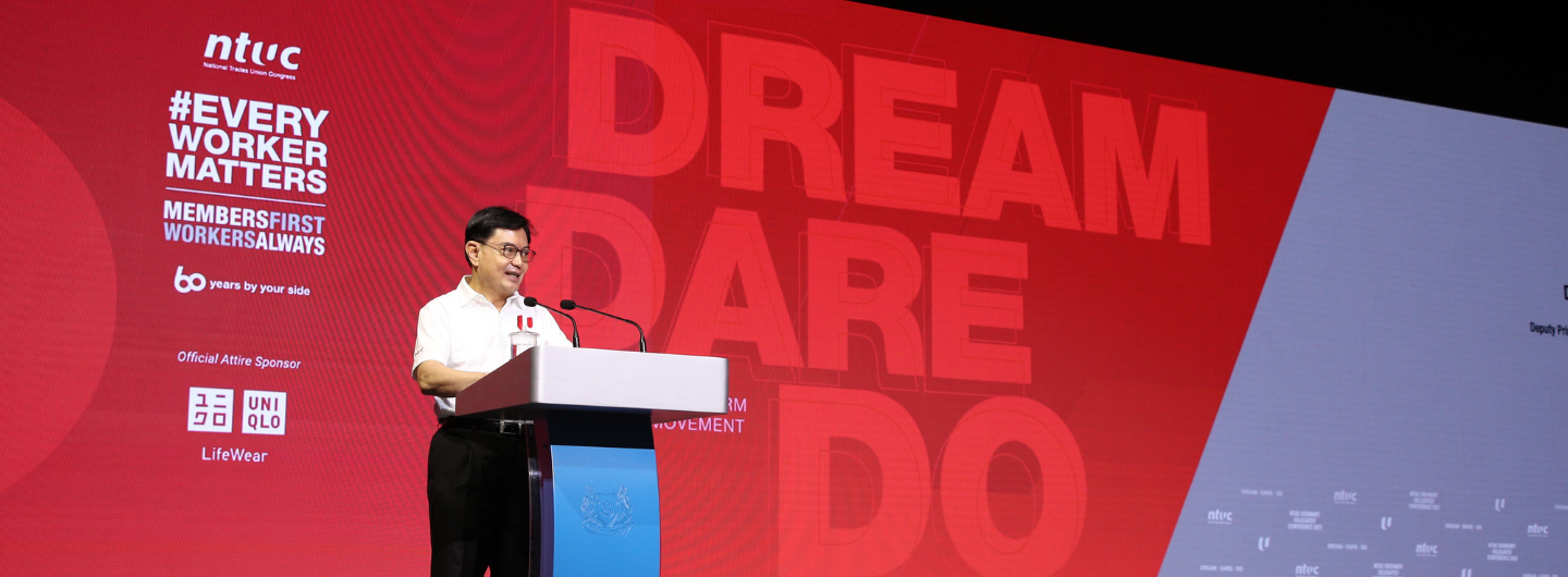 Speaker at podium with NTUC backdrop: "#EVERYWORKERMATTERS", "DREAM DARE DO", and UNIQLO logo.